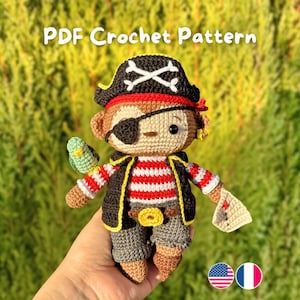 Peut inclure: Une poupée singe pirate au crochet avec un chapeau noir, un cache-œil et une chemise rayée rouge et blanche. La poupée a un petit perroquet vert sur le bras et tient un petit papier. Le texte "PDF Crochet Pattern" est en haut.