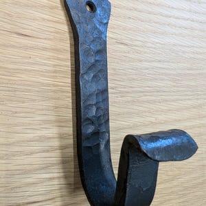 以下が含まれることがあります： ハンマー仕上げの黒い金属製のフック。フックは湾曲したデザインで、上部に小さな穴が開いており、吊り下げることができます。