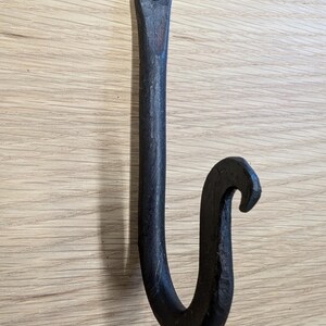 May include: Black metal hook with a curved design. The hook is mounted on a wooden surface.