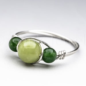 May include: A silver ring with three green stones. The center stone is a larger, light green stone, and the two stones on either side are smaller, darker green stones.