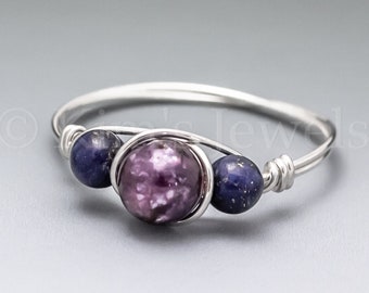 May include: A silver ring with a purple and white gemstone and two blue gemstones. The ring is made with wire wrapping.