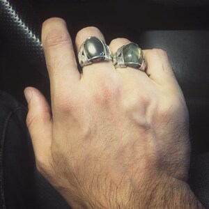 May include: Two silver rings with dark green oval stones. The rings are on a person's hand.