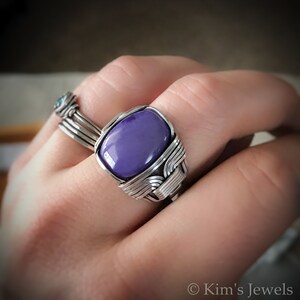 May include: A silver wire wrapped ring with a purple gemstone. The ring is on a person's finger.