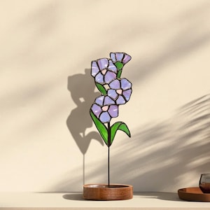 May include: A stained glass flower sculpture with three purple flowers and green leaves on a wooden base.