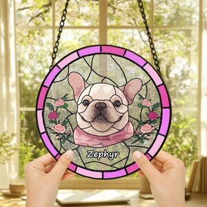 May include: A stained glass window hanging featuring a pink and white French Bulldog with the name "Zephyr" written below. The dog is surrounded by pink roses.