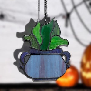 Op de afbeelding: Gebrandschilderde glazen vetplant in een blauwe pot, hangend aan een zwarte ketting. De plant heeft groentinten, de pot blauwe en paarse tinten. Ontworpen als raamdecoratie.