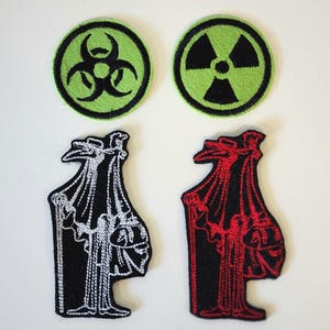 May include: Four embroidered patches including two circular patches with lime green backgrounds featuring a black biohazard symbol and a black radiation symbol, and two plague doctor figures, one outlined in white and one outlined in red.