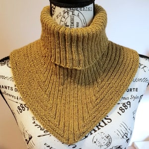 Könnte beinhalten: Ein gestrickter Schal in senfgelber Farbe. Der Schal ist umgeklappt, um einen Rollkragen-Stil zu erzeugen.