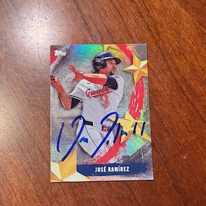 May include: A baseball card featuring José Ramírez in a Cleveland Guardians uniform. The card has a holographic background with star accents and a printed signature. The player is in a batting stance, with the word "Guardians" visible on the jersey.