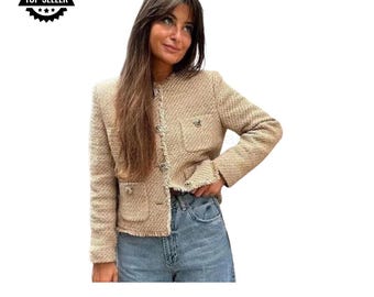 May include: A beige tweed cropped jacket with a frayed hem and gold button accents. The jacket has two flap pockets and a button closure.