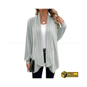 May include: A light gray ribbed cardigan with a draped collar and a front zipper. The long-sleeved sweater is worn over a white top and black pants. A black purse with a gold chain is held in the left hand. The text "Autumn-" is visible on the left side.