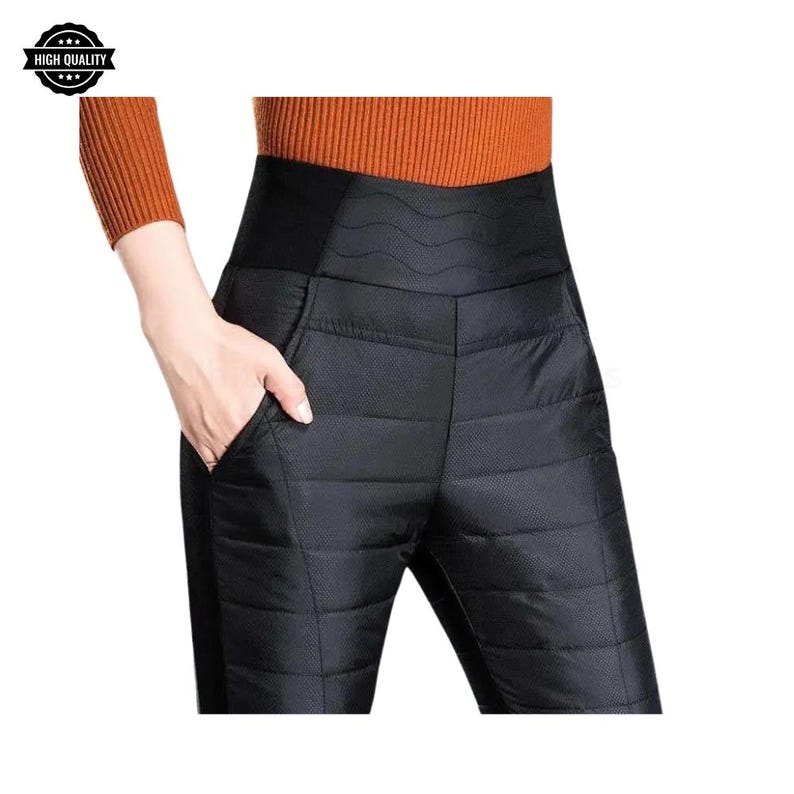Pode incluir: Cal&ccedil;as pretas acolchoadas com cintura alta e bolsos. As cal&ccedil;as t&ecirc;m um padr&atilde;o costurado horizontal e uma cintura larga. A imagem tamb&eacute;m mostra uma pessoa com uma camisa marrom de manga comprida. A imagem tem um logotipo "HIGH QUALITY".