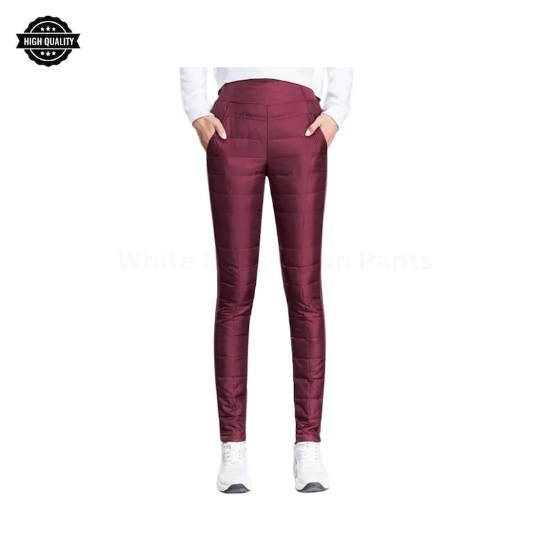 Pode incluir: Cal&ccedil;as de penas acolchoadas bord&ocirc; com cintura alta e bolsos. As cal&ccedil;as s&atilde;o mostradas com t&ecirc;nis brancos. A imagem tem um logotipo "High Quality". O texto "White Down Pants" &eacute; vis&iacute;vel.