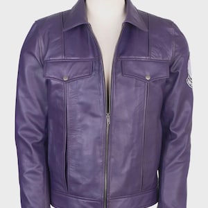 May include: A purple leather jacket featuring a classic collar, a full-length front metal zipper, and two chest pockets with buttoned flaps. The jacket includes vertical seam detailing and a circular patch on the left sleeve with visible text.