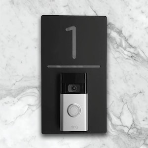 Può includere: Un supporto per campanello nero con il numero "1" e un campanello Ring argentato.