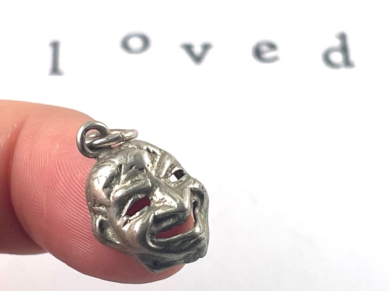 This vintage silver mask charm features the expressive details of a drama mask, symbolizing comedy and tragedy. Its intricate design and timeless patina make it perfect for performing arts lovers or anyone seeking a unique, symbolic jewelry piece.