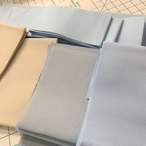 May include: Stacks of beige and blue Aida cloth fabric for cross stitch projects.