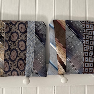 May include: Two zippered pouches made from repurposed neckties. The pouch on the left has a brown and blue color scheme. The pouch on the right has a blue and brown color scheme.