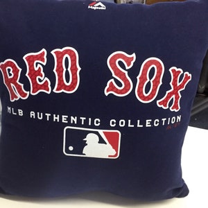 May include: A blue pillow with the words "RED SOX" in red and white lettering. The pillow also has the MLB Authentic Collection logo and the Majestic logo.
