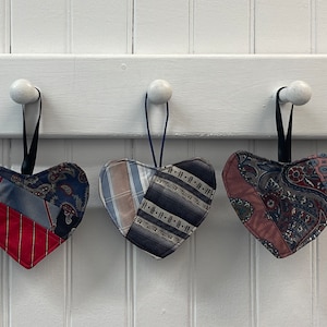 May include: Five handmade heart-shaped ornaments made from repurposed fabric. Each ornament is a different color and pattern, including blue, red, and brown.
