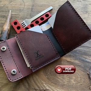 May include: A dark burgundy leather wallet featuring a fold-over design with two silver-toned metal snap buttons, visible stitching, and the black printed logo locasin. The wallet contains white cards and is positioned near a red metal tool.