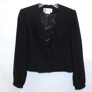 May include: A black blazer with a V-neckline and long sleeves. The blazer has a single-button closure and a small pocket on the front. The interior lining features a repeating pattern of the word "Prophecy".