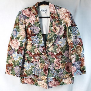 May include: A long-sleeve blazer featuring a dense, multi-colored floral tapestry pattern with shades of pink, blue, green, and brown. The garment has a notched lapel, a single-button front closure, two front pockets, and a solid white interior lining.