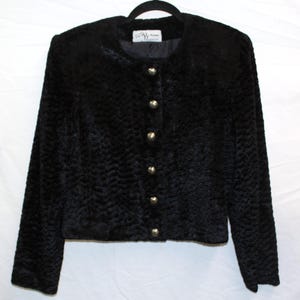 May include: A black textured jacket with a round collar and long sleeves. The jacket has six gold-colored buttons down the front. The jacket is hanging on a black hanger.
