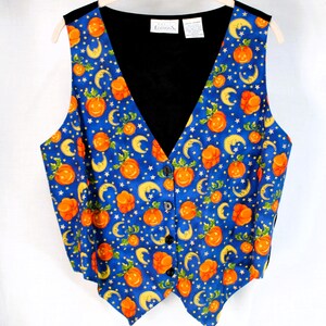 Puede incluir: Un chaleco sin mangas con un fondo azul vibrante y un patrón repetitivo de calabazas naranjas, lunas crecientes amarillas y pequeñas estrellas blancas. La prenda tiene un cuello en V negro, cuatro botones negros y un forro interior negro.