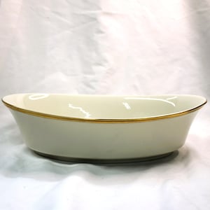 Könnte beinhalten: Cremefarbene ovale Servierschüssel mit Goldrand. Die Schüssel hat eine glatte, glänzende Oberfläche und ein schlichtes, elegantes Design. Die Schüssel ist wahrscheinlich aus Keramik oder Porzellan.