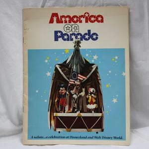Puede incluir: Un folleto de recuerdo vintage titulado "America on Parade" con un fondo azul y estrellas blancas. La portada presenta personajes de dibujos animados en una carroza. El texto "America on Parade" está en rojo y azul.