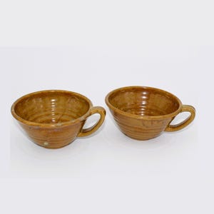 Puede incluir: Dos tazas de cerámica marrón con un diseño texturizado y en espiral. Las tazas tienen una forma redondeada y un solo asa.