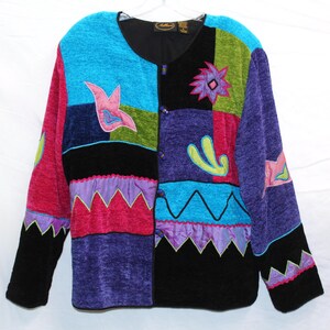 May include: A colorful patchwork jacket with a variety of textures and shapes. The jacket features a mix of blue, pink, green, purple, and black panels, with embroidered floral and geometric designs. It has long sleeves and a button-up front.