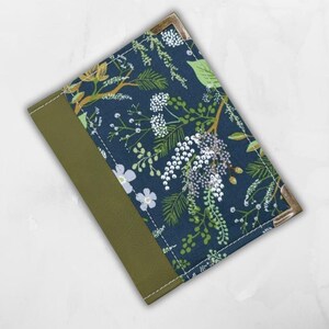 May include: A rectangular journal with a dark blue floral pattern cover and olive green spine. The floral design includes white, green, and yellow accents. The corners are reinforced with gold-coloured metal. The journal is closed.