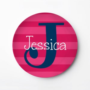 May include: A pink and navy blue personalized plate with the letter J and the name Jessica in white.