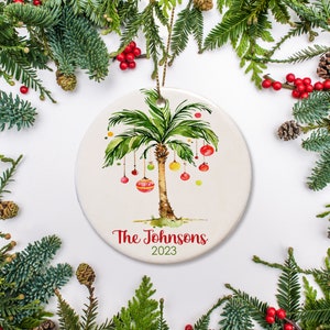 A palm tree decorated with ornaments is featured on this ceramic ornament. It includes a name and date.