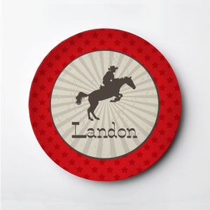 May include: Red and white personalized plate with a silhouette of a cowboy riding a horse. The plate says "Landon" in a brown font.