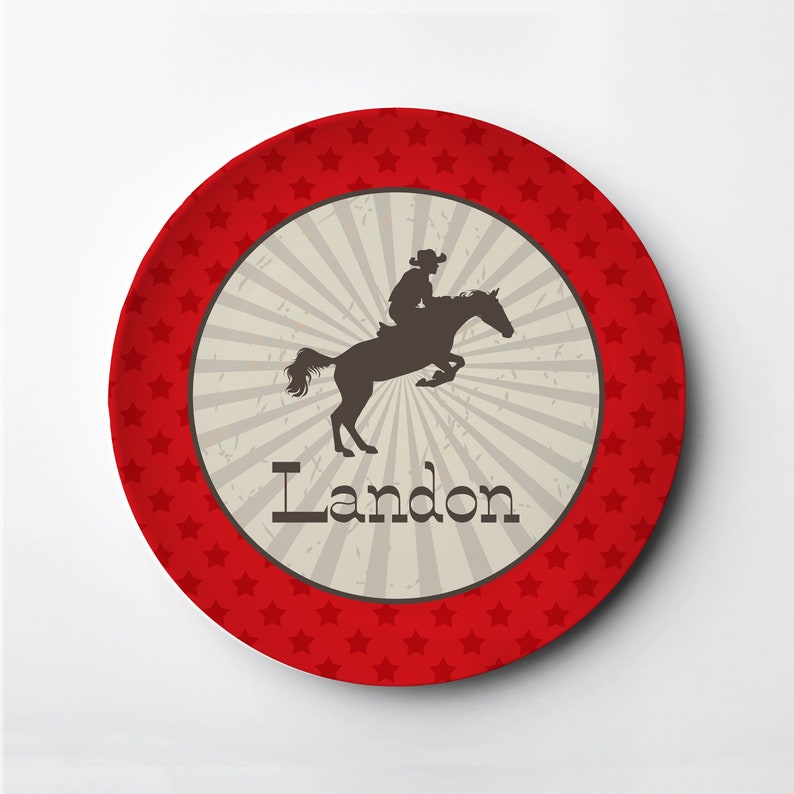 May include: Red and white personalized plate with a silhouette of a cowboy riding a horse. The plate says "Landon" in a brown font.