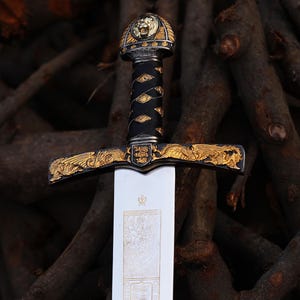 May include: A decorative sword with a gold lion head pommel and gold accents on the hilt and guard. The blade is silver and has a decorative design.
