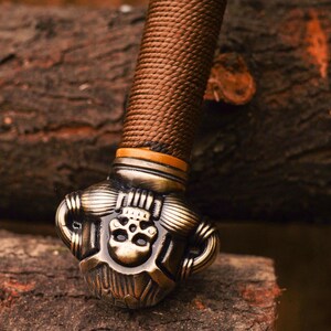 May include: Close-up of a sword pommel with a detailed skull design. The pommel is made of metal and has a brown leather wrap.