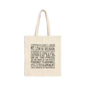 May include: A cream-coloured tote bag with black text. The text reads: "Congress shall make no law respecting an establishment of religion, or prohibiting the free exercise thereof; or abridging the freedom of speech, or of the press..."