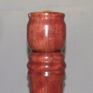 May include: A wooden salt and pepper shaker set with a dark reddish-brown finish. The shakers are made of wood and have a cylindrical shape.