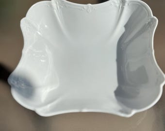 May include: A white porcelain serving bowl with a decorative, scalloped rim and a raised floral design.