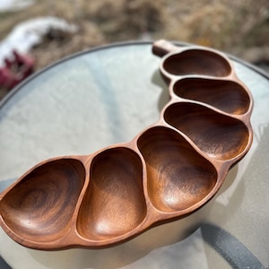 May include: A wooden serving tray with multiple compartments, ideal for snacks or appetizers. The tray is made of a rich, dark brown wood and has a curved, organic shape. The compartments are various sizes and shapes, perfect for a variety of foods.