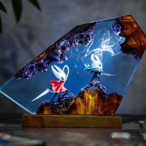 May include: A resin art piece featuring two stylized figures in a battle scene. The figures are set against a blue backdrop with swirling white accents, encased in a clear, angled resin block. The base is a wooden rectangle.