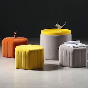 May include: A selection of contemporary furniture. Features a round side table with a yellow top, three ottomans in orange, yellow, and grey, and a decorative bird ornament. The ottomans are upholstered.
