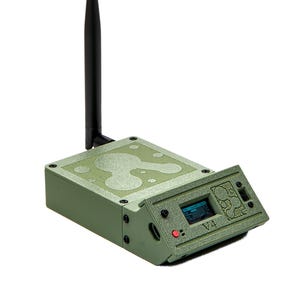 May include: An olive green electronic device with a black antenna. The device has a small screen displaying information and a red button. The text "V4" is visible on the front panel. The device has a textured surface.