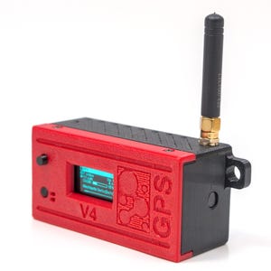 Peut inclure: Appareil GPS rouge et noir avec un petit écran affichant des données. L'appareil est équipé d'une antenne noire et le texte "GPS V4" est visible. L'appareil a un petit écran affichant des données.