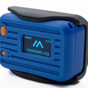 May include: A blue electronic device with a black protective cover. The device has an orange button and a small screen displaying the text "UNSET", a logo, and "meshtastic.org". The date "2.3.12" is also visible on the screen.