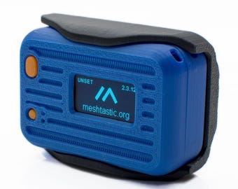 May include: A blue electronic device with a black protective cover. The device has an orange button and a small screen displaying the text "UNSET", a logo, and "meshtastic.org". The date "2.3.12" is also visible on the screen.
